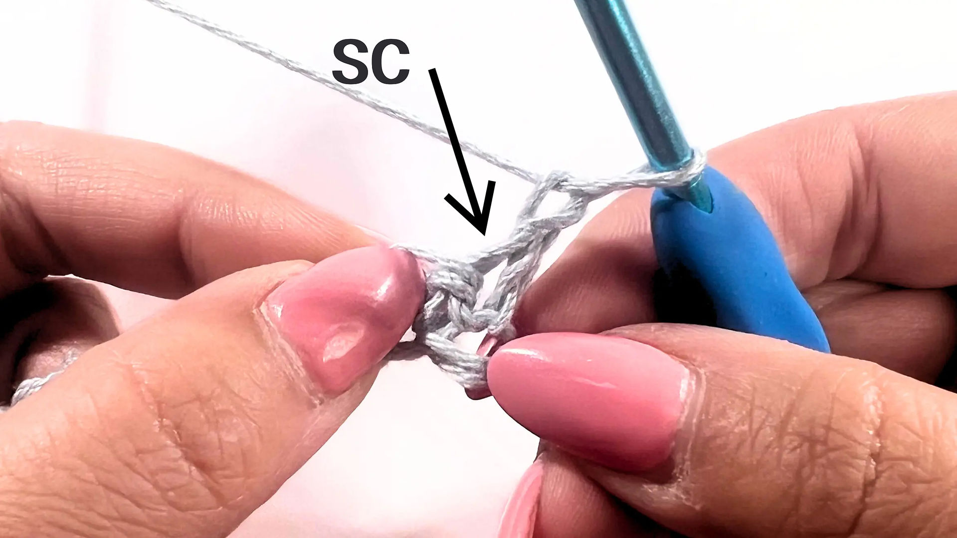 Close-up showing where to work the first single crochet of the second row—into the very first stitch. An arrow points directly at the top of that stitch