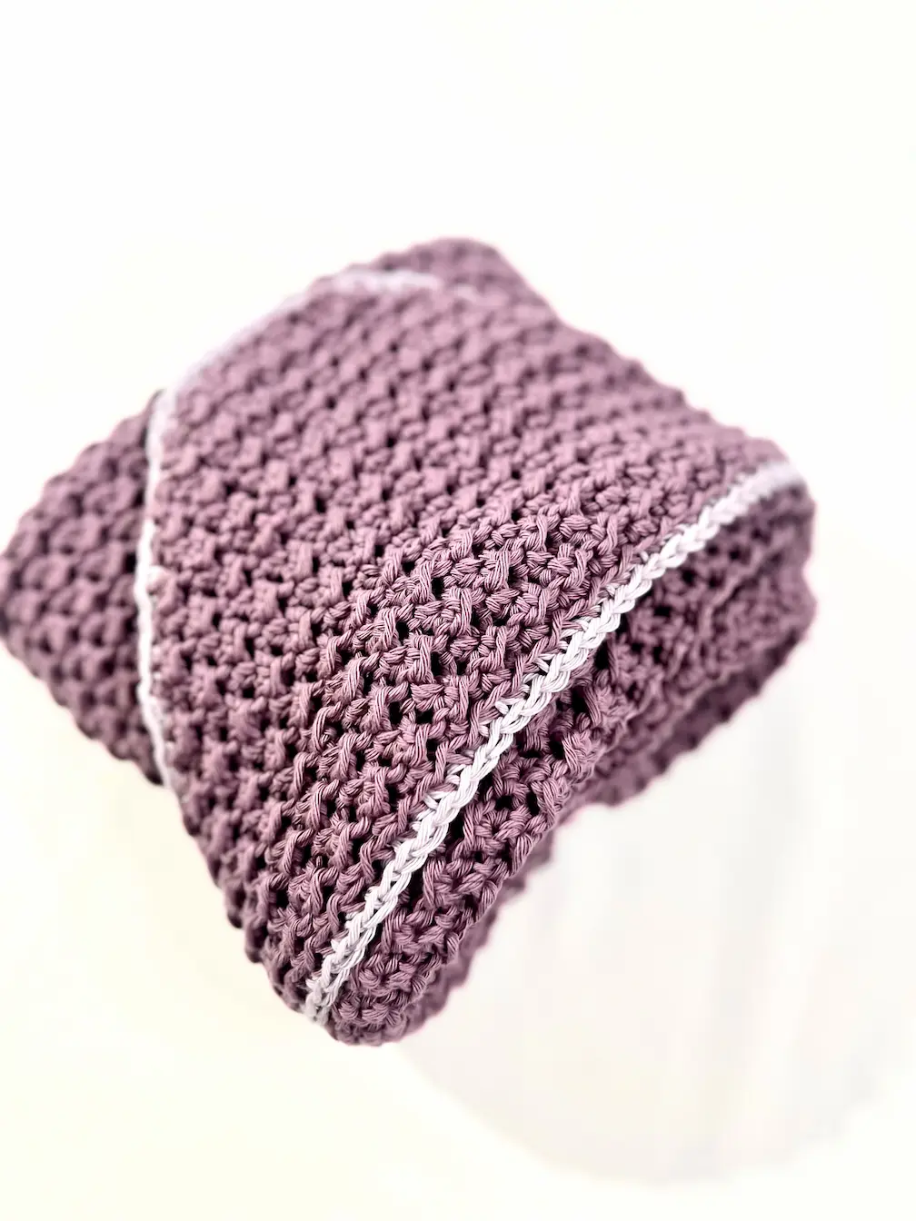 Close-up of the folded Snuggle Hooded Baby Towel, highlighting the textured C2C Even Moss Stitch and crisp edging in contrasting grey yarn. The hood corner rests gently over the top.