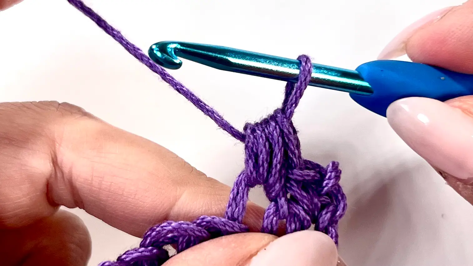 Hook pulling through all loops on the hook to complete the Bean Stitch, showing tension and forming a puffed texture.