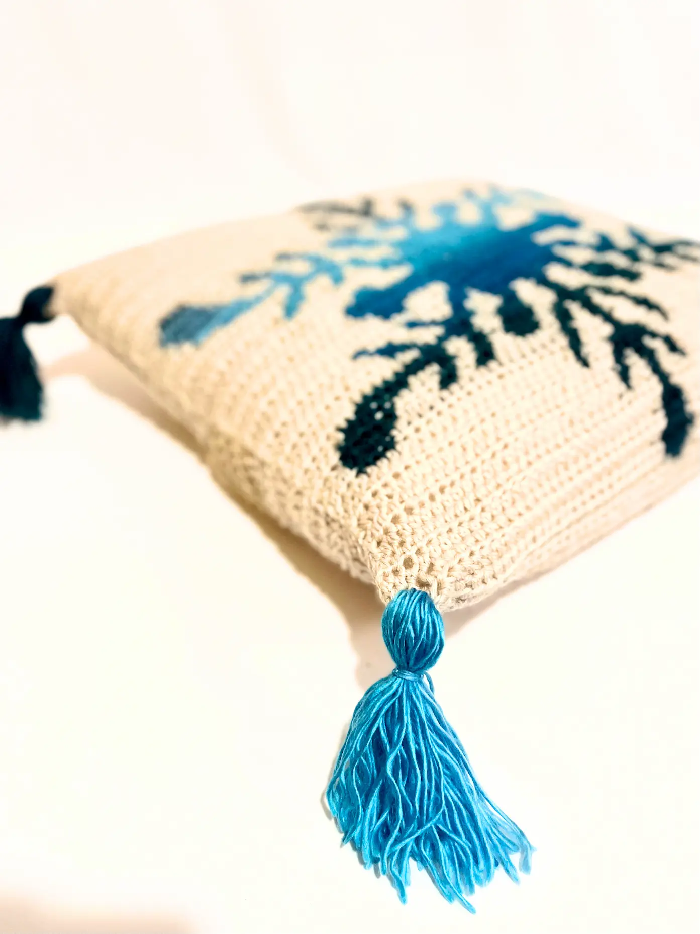Crochet Northern Flakes Pillow laying on a white background with blue gradient snowflake and tassels.