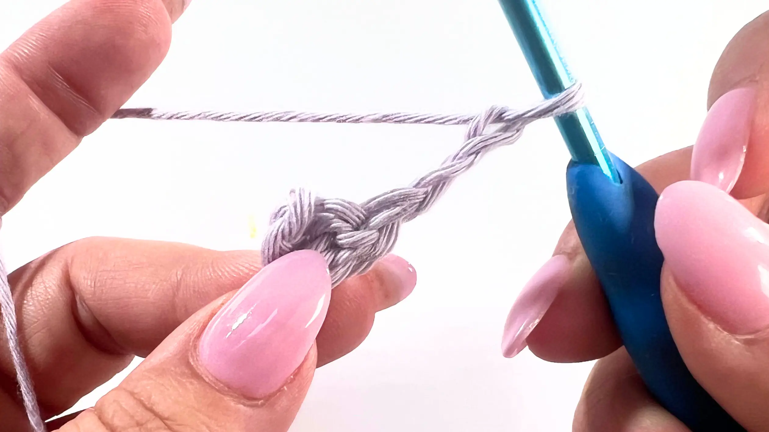 Crochet hook and yarn forming a chain to continue the Lemon Peel Stitch C2C baby washcloth pattern in light purple cotton yarn.