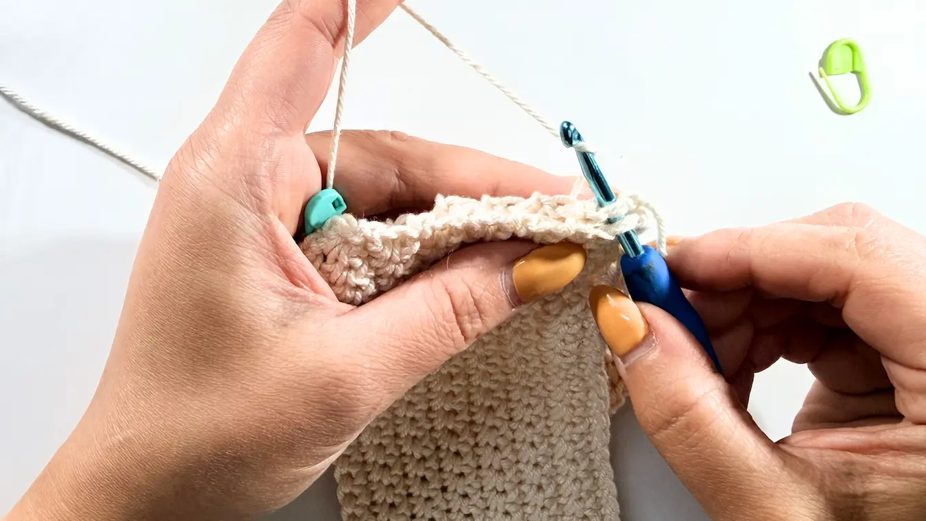 Close-up of a crochet hook joining two crochet panels together with single crochet stitches.