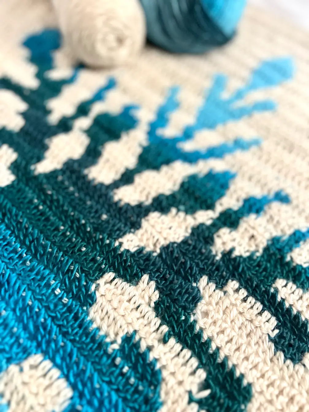 Detail shot of the Northern Flakes crochet blanket with yarn in the background, highlighting the blue snowflake stitches.