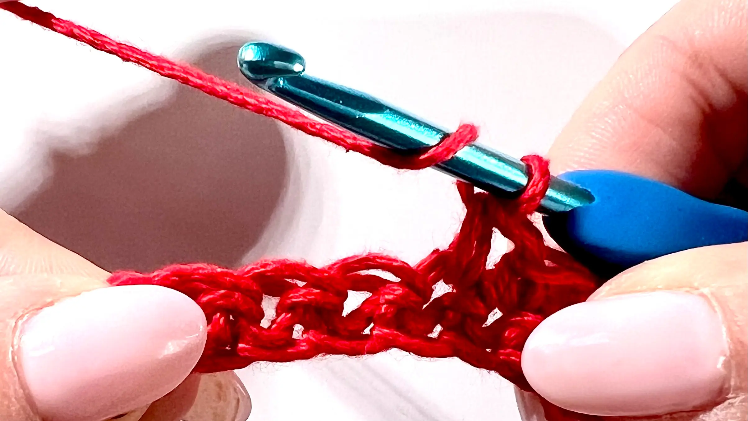 Crocheter creating a puff stitch with red yarn, showing yarn overs and multiple loops on hook before pulling through.