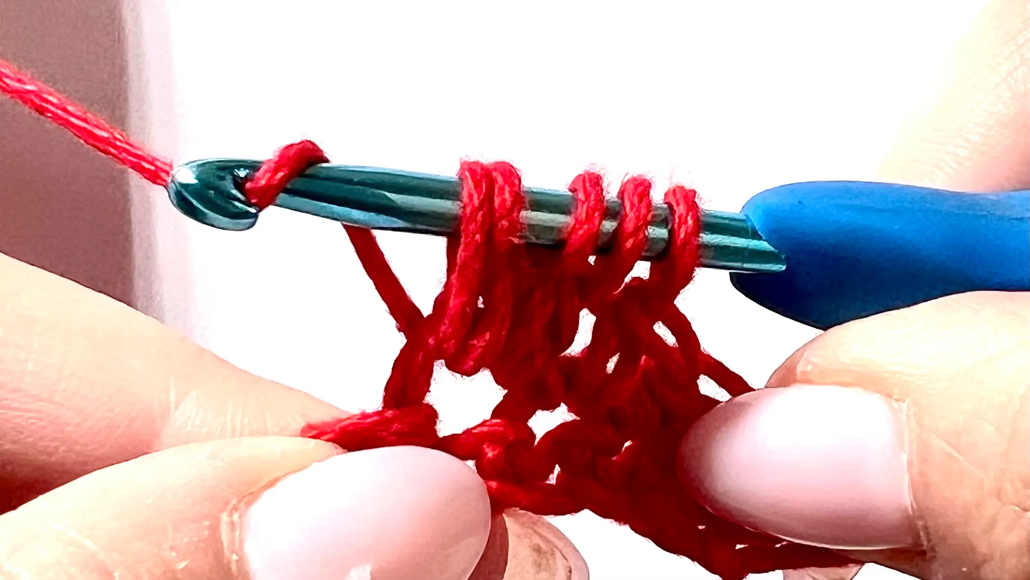 Crocheter forming a bobble stitch in red yarn, with several incomplete double crochets on hook before closing the cluster.
