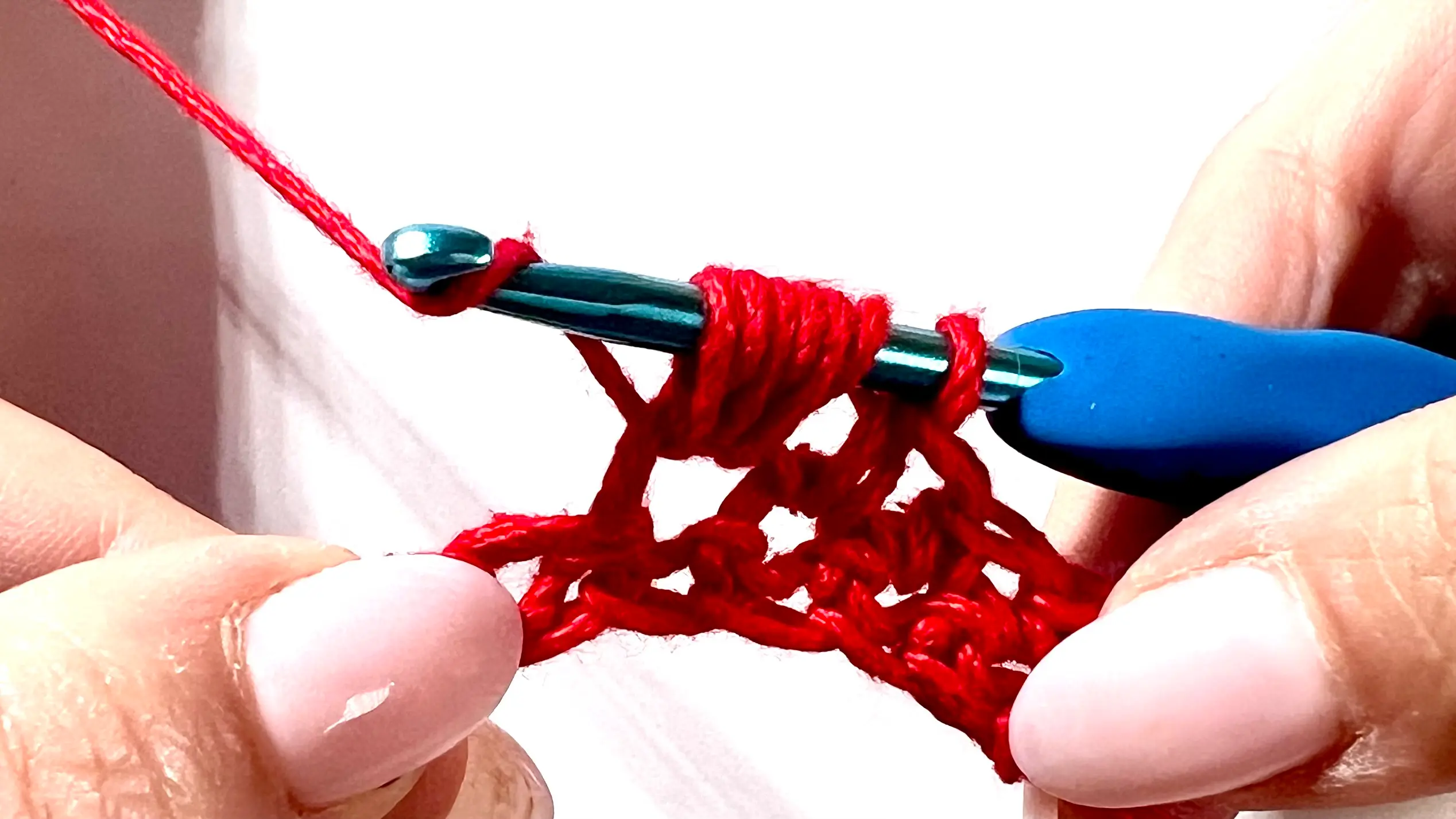 Crocheter creating a puff stitch with red yarn, showing yarn overs and multiple loops on hook before pulling through.