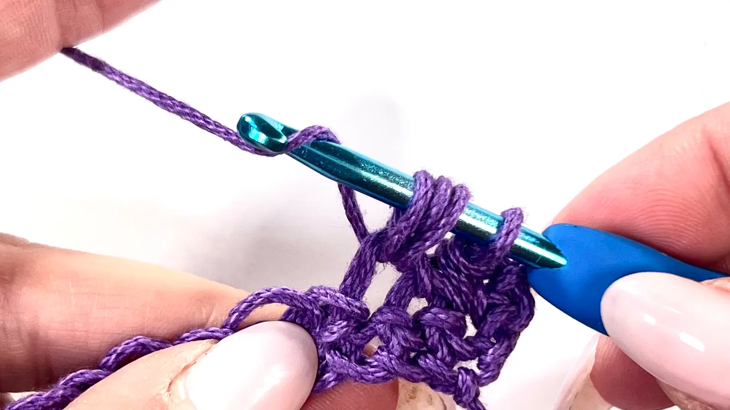 Crocheter pulling up multiple loops in the same stitch for the Bean Stitch, building texture with purple yarn on a blue crochet hook.