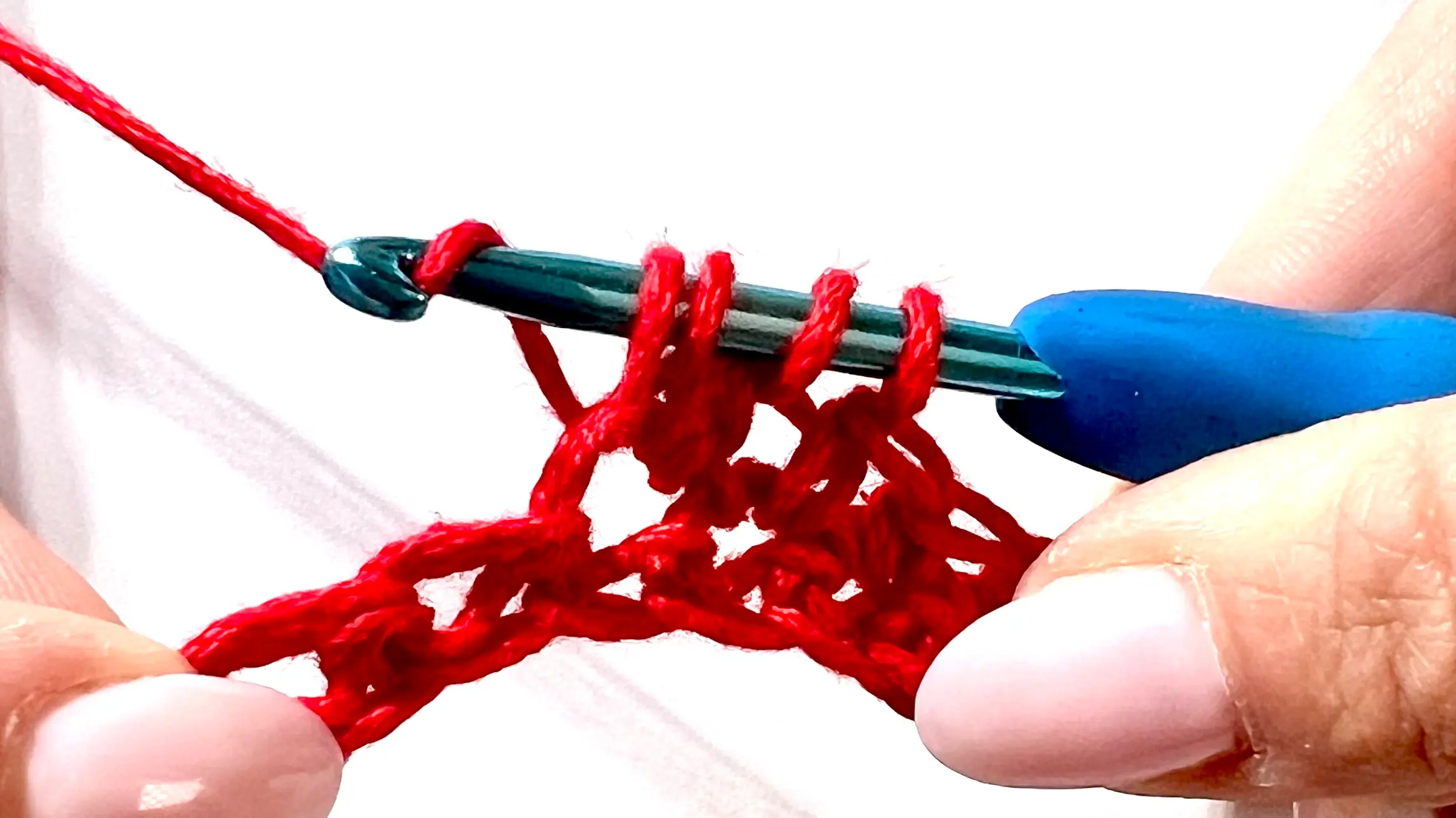 Crocheter forming a bobble stitch in red yarn, with several incomplete double crochets on hook before closing the cluster.
