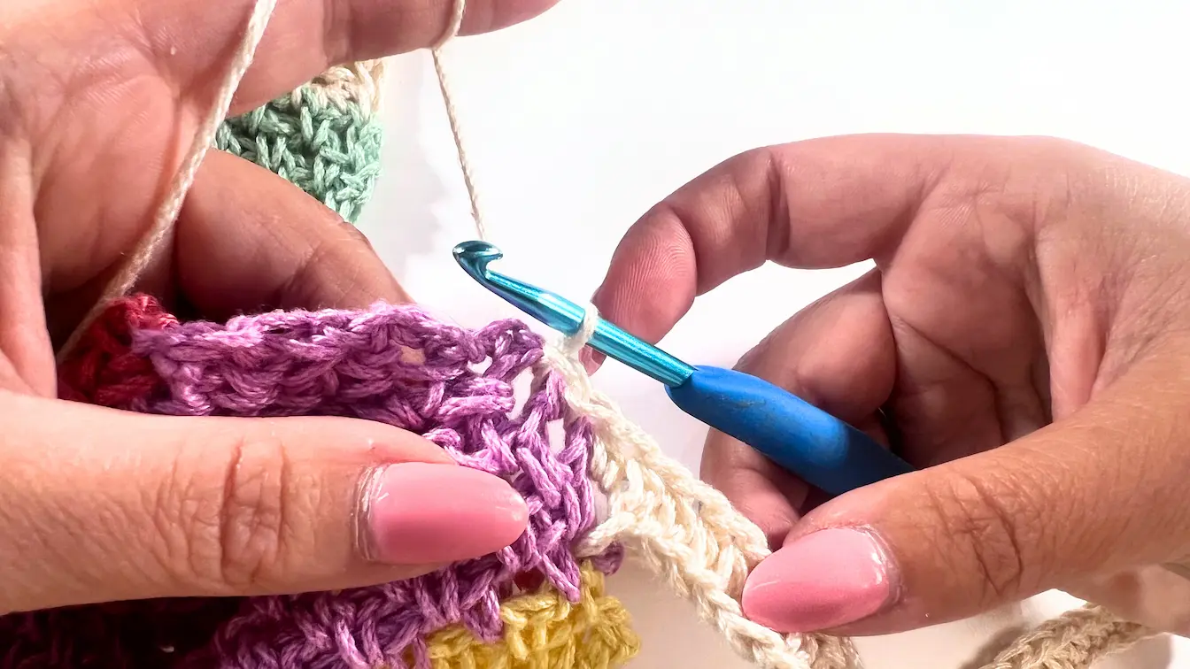 Crochet hook working across the newly attached foundation chain row, crocheting the first row of the sleeve to join it to the panel edge.