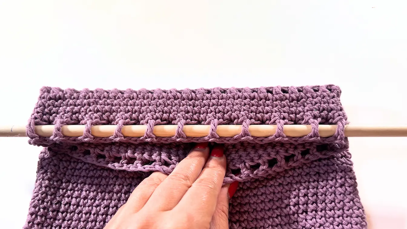 Crochet wall organizer with wooden dowel secured through top row of stitches.