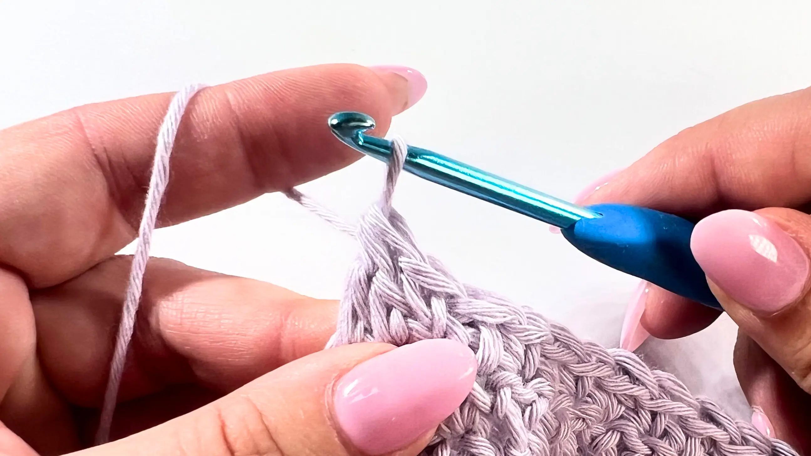 Crochet hook completing DC2tog by pulling through the last three loops, finishing the decrease at the end of the row in Lemon Peel Stitch C2C baby washcloth.
