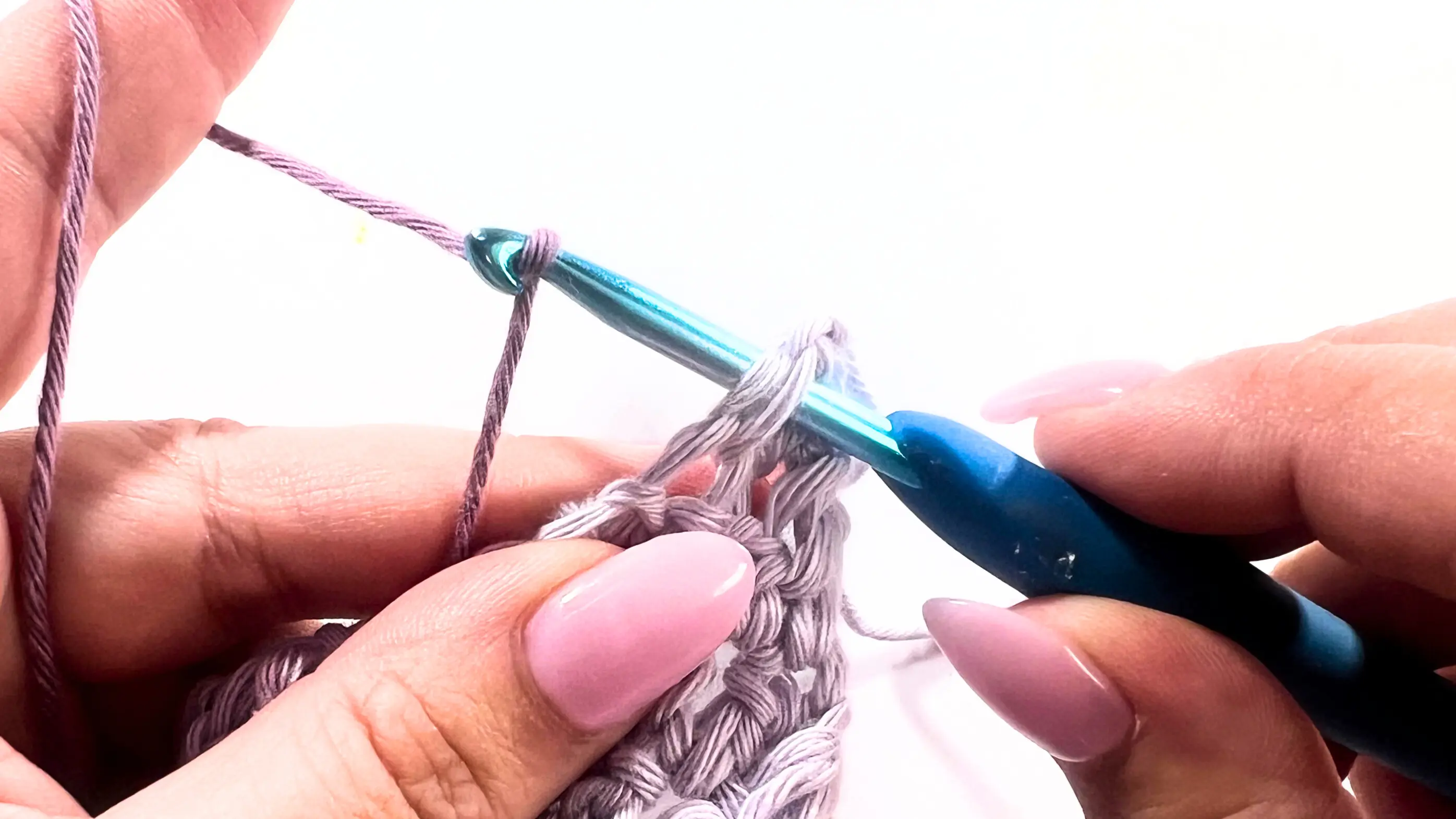 Close-up of crochet hook inserting into the first stitch of the washcloth while adding a new yarn colour to begin the Picot Border.
