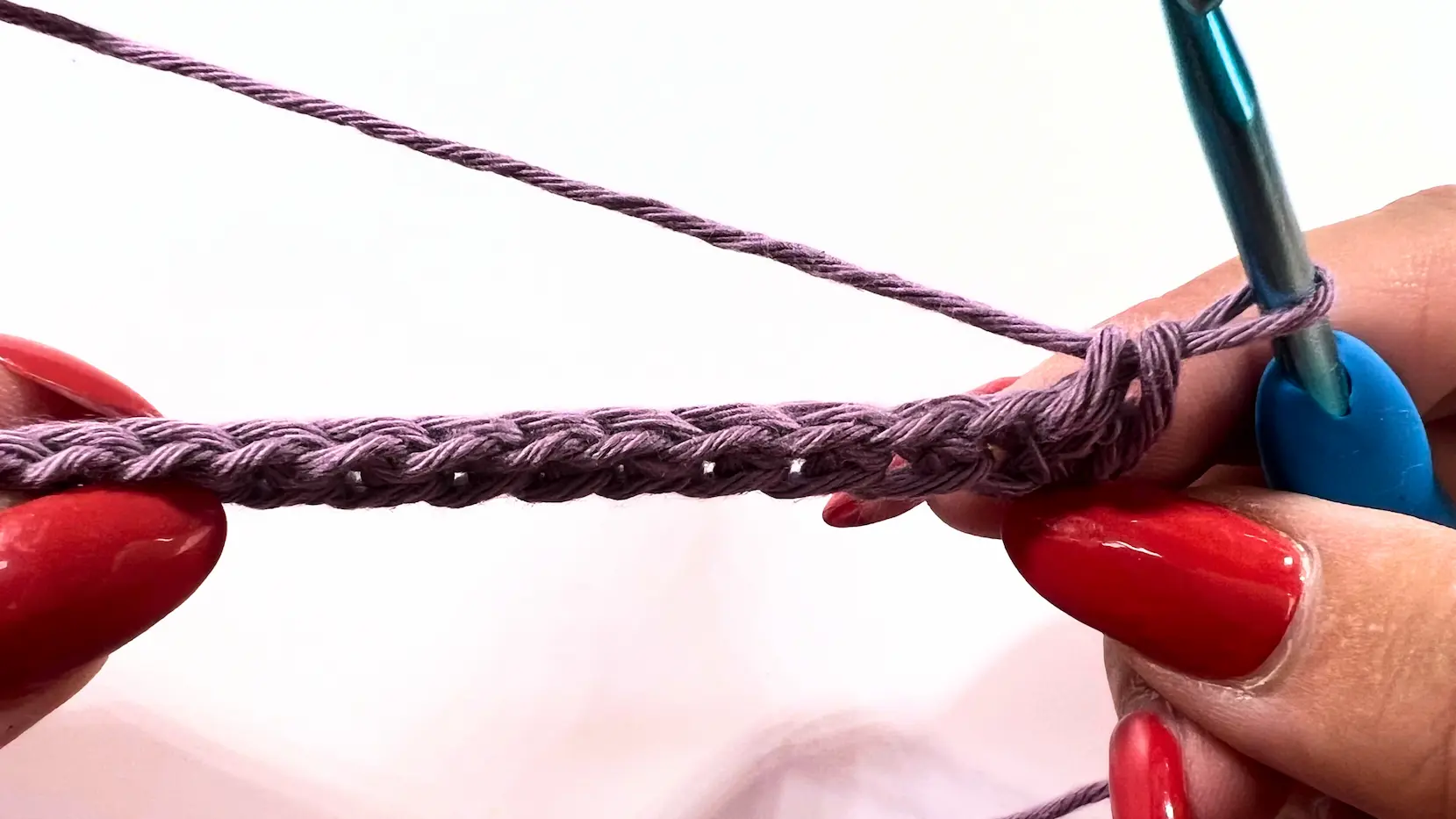 Foundation chain held with crochet hook, showing stitch detail in purple yarn.