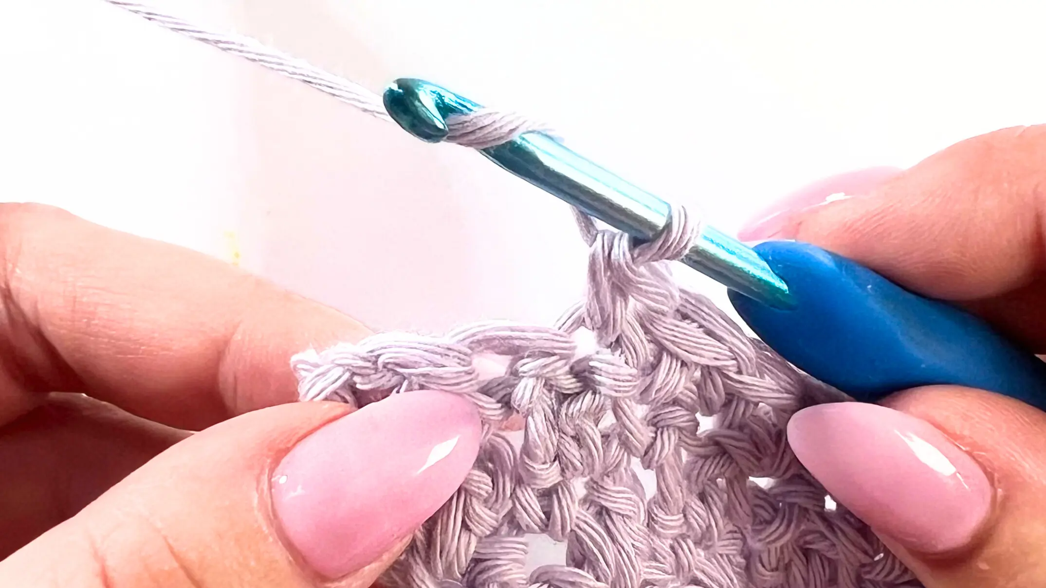 Crochet hook with yarn over positioned just before inserting into the second-to-last stitch of the Lemon Peel Stitch C2C baby washcloth.