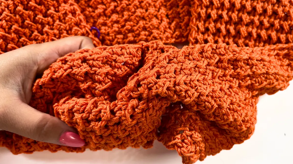 Hands holding edges of the crochet fabric, aligning them to complete the twist in the summer top.