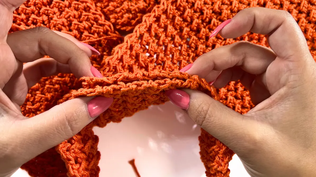 Hand holding the center section of the crochet rectangle, beginning to fold and twist the fabric for the summer top design.