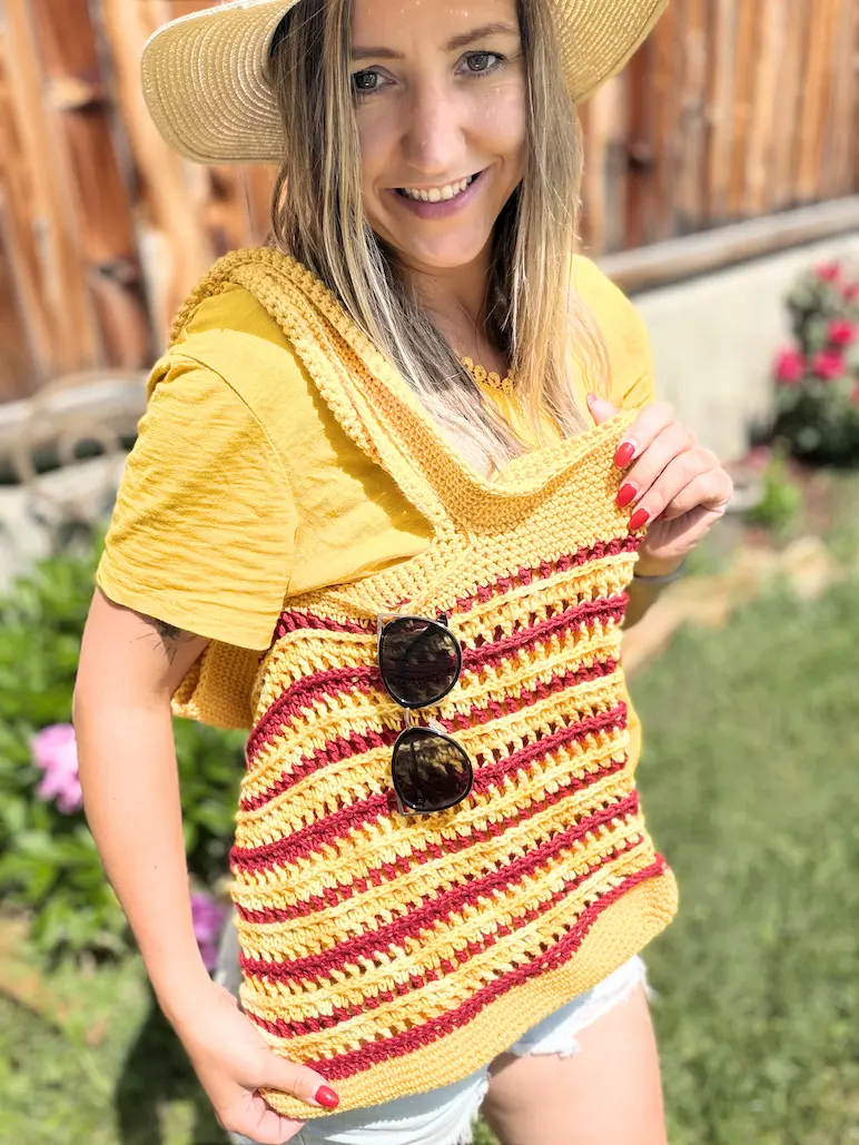 Woman wearing a handmade crochet summer beach tote bag over her shoulder, showcasing the finished striped tote pattern in yellow and burgundy yarn.