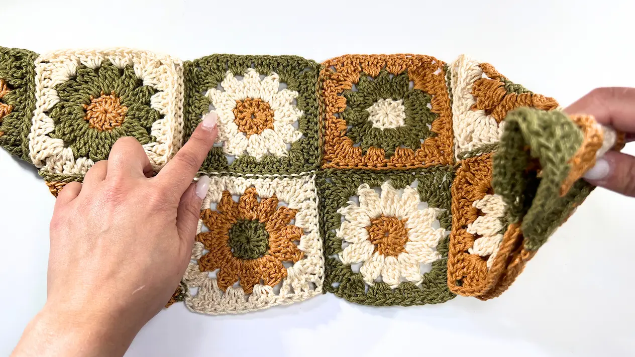 Hands holding the edges of the folded crochet piece, starting to bring the corners together for seaming.