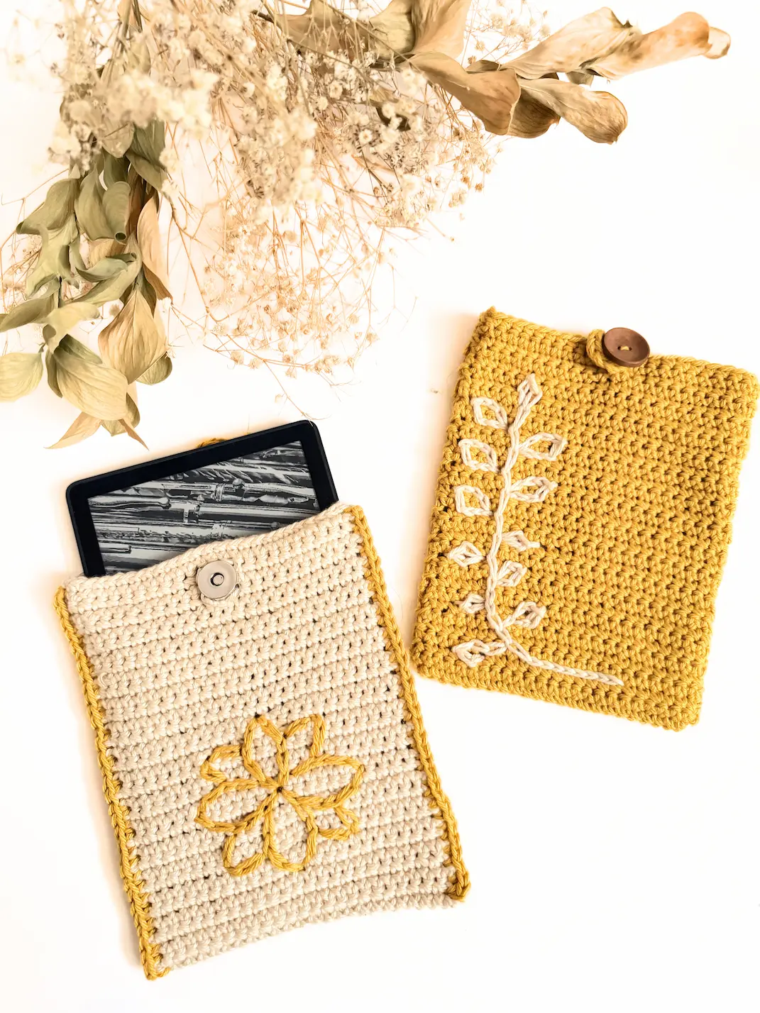Cream crochet Kindle sleeve with mustard edging and a floral surface crochet design, shown partially holding a Kindle e-reader.