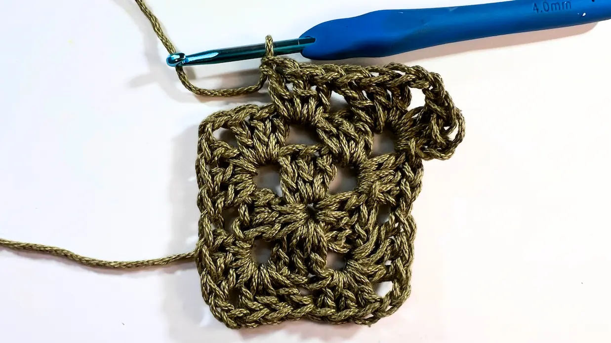 Granny square with one new 3 double crochet cluster worked along the side between two corners.