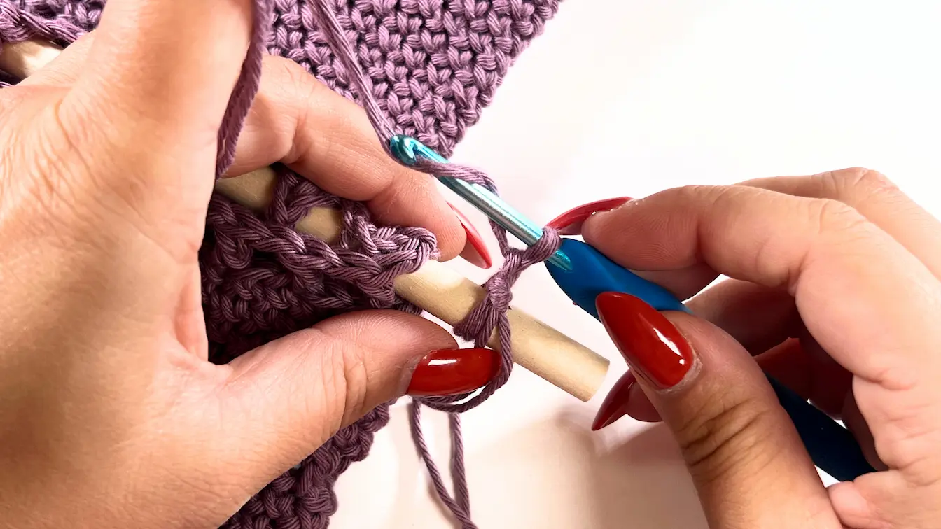 Crochet hook working double-stranded foundation chain around wooden dowel.