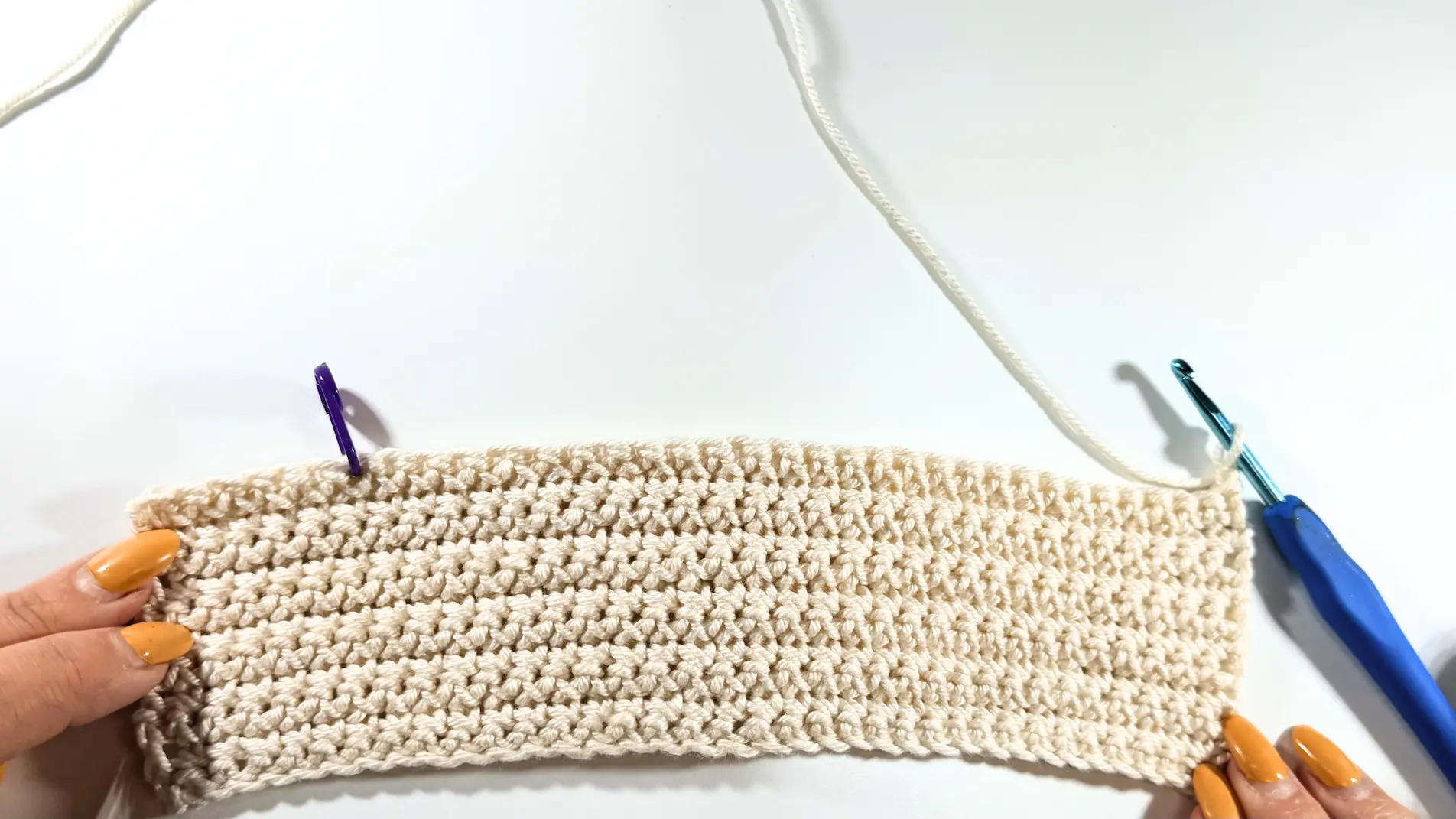 Long crochet rectangle with a stitch marker placed near one end and a crochet hook attached to the working yarn.