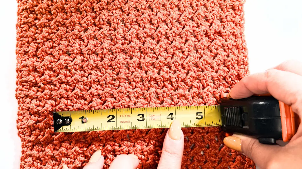 Measuring crochet gauge swatch width with tape measure to count stitches