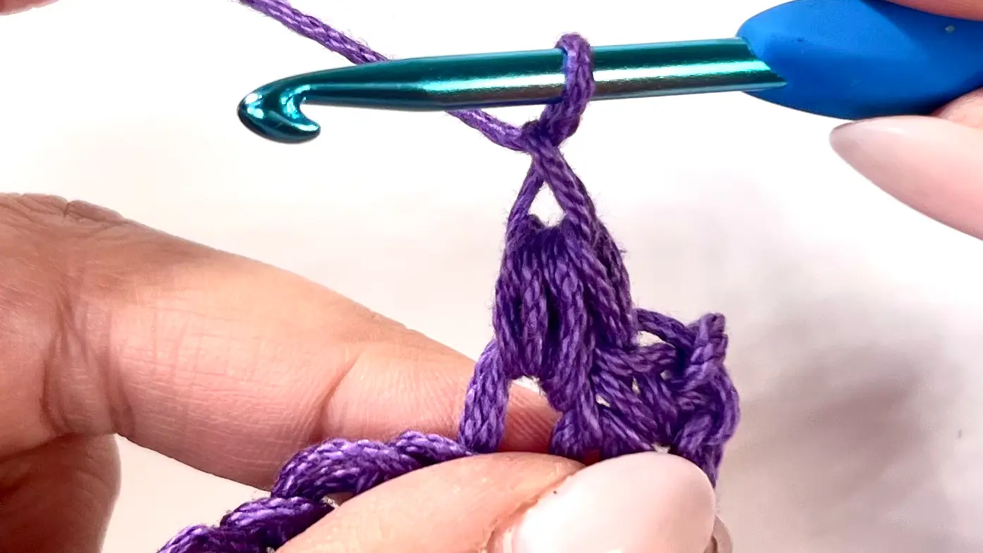 Crocheter yarning over to chain one after completing the Bean Stitch, ready to start the next stitch in the row.