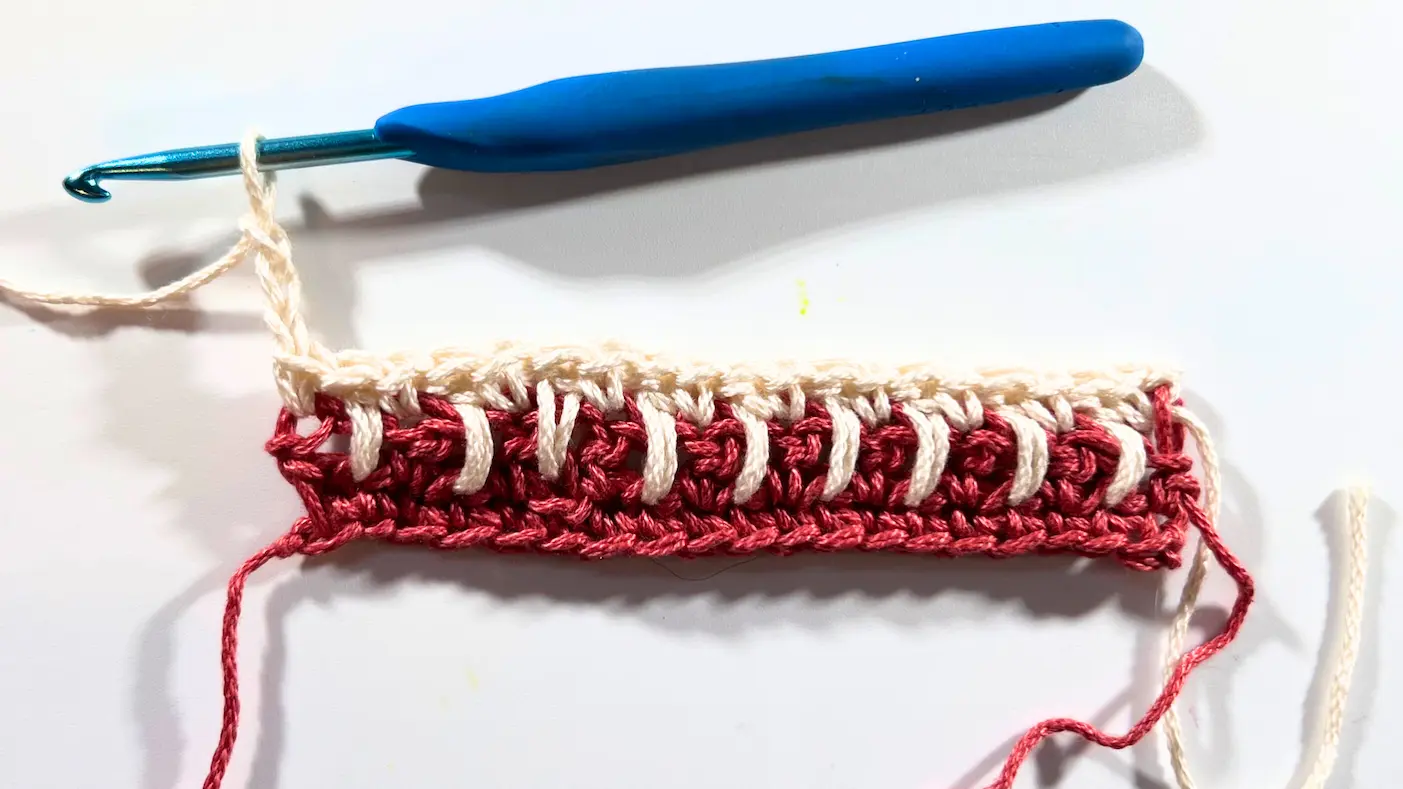 Crochet swatch with cream yarn row finished in spike stitches. At the edge, three chains are worked to begin the next row.