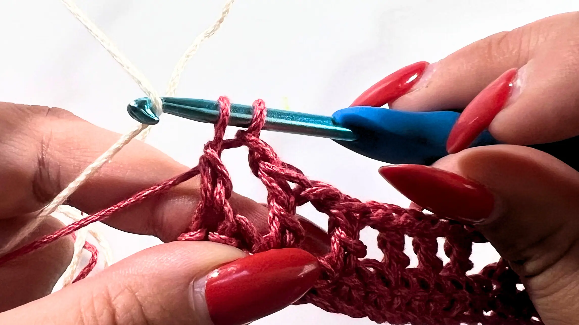 Close-up of crochet swatch showing cream yarn placed on the hook to finish the last double crochet in place of the red yarn.