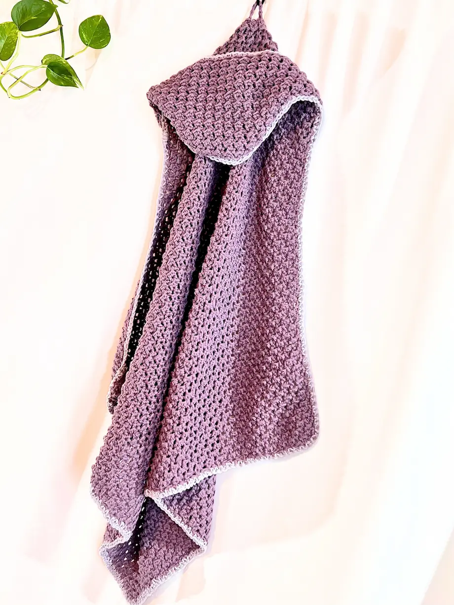 The finished Snuggle Hooded Baby Towel laid flat with the hood folded over, showing the full square shape and textured body. The light grey edging adds a clean finish to the dusty lavender crochet.
