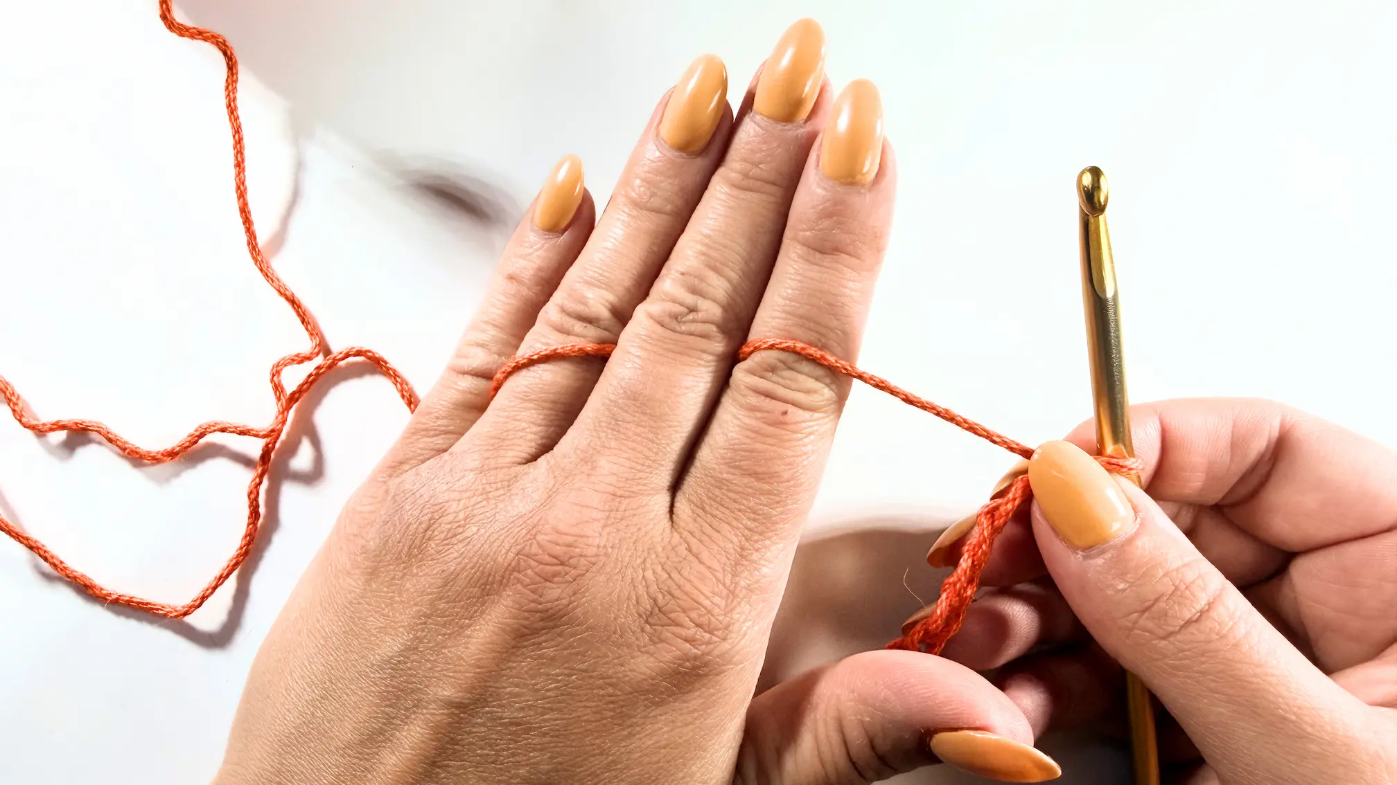 Hands demonstrating a simple crochet yarn hold with yarn placed between fingers for relaxed tension.