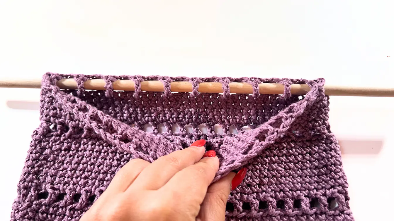 Hand weaving wooden dowel through crochet stitches to attach organizer.