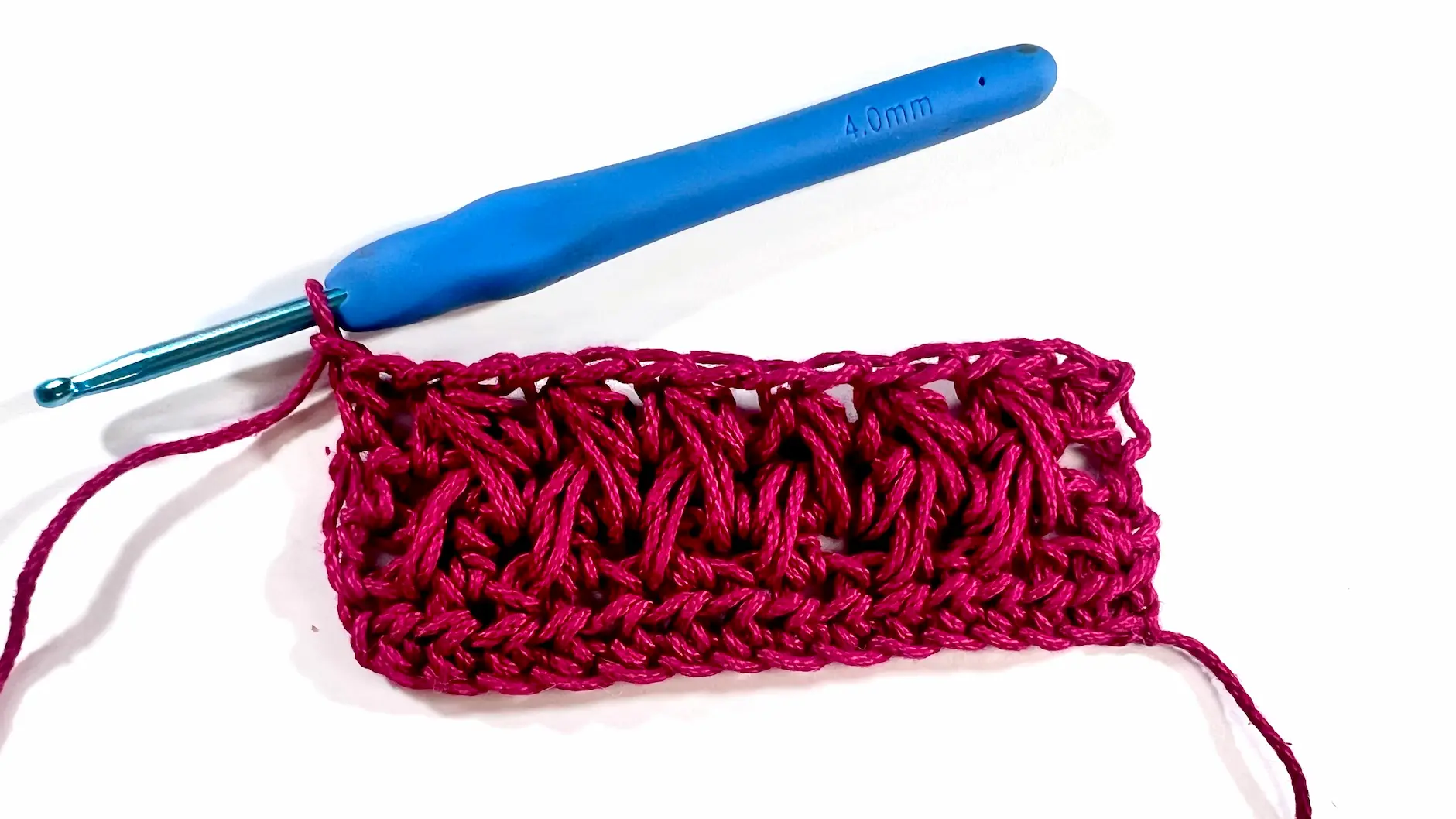 Close-up showing how to crochet the feather stitch step-by-step using fuchsia yarn and a blue crochet hook — part of a textured stitch tutorial.