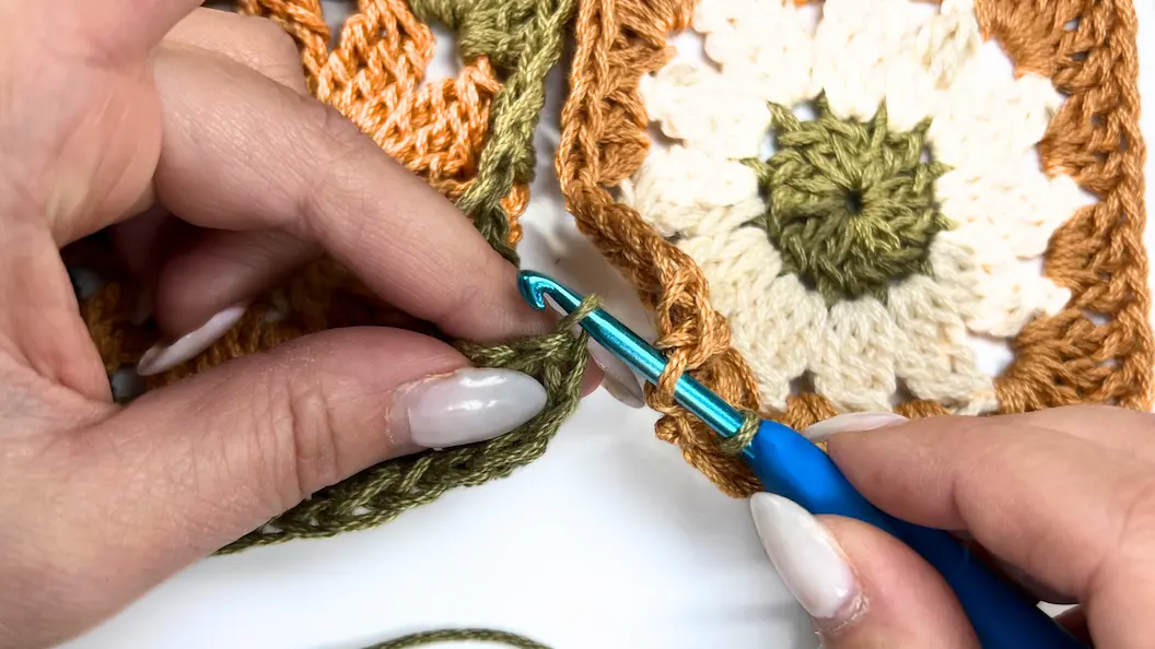 Crocheting across the edges of two granny squares using the slip stitch method with green yarn.