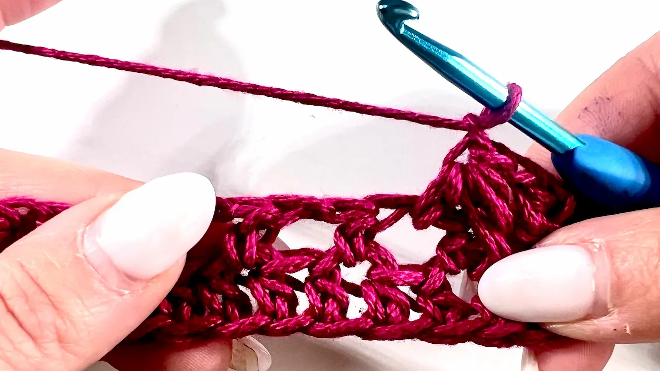 Close-up showing how to crochet the feather stitch step-by-step using fuchsia yarn and a blue crochet hook — part of a textured stitch tutorial.