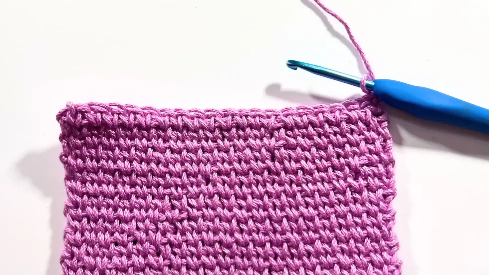 Close-up photo of a pink crochet swatch made with the Waistcoat Stitch, also known as the Knit Stitch, worked with a blue ergonomic crochet hook on a white background.