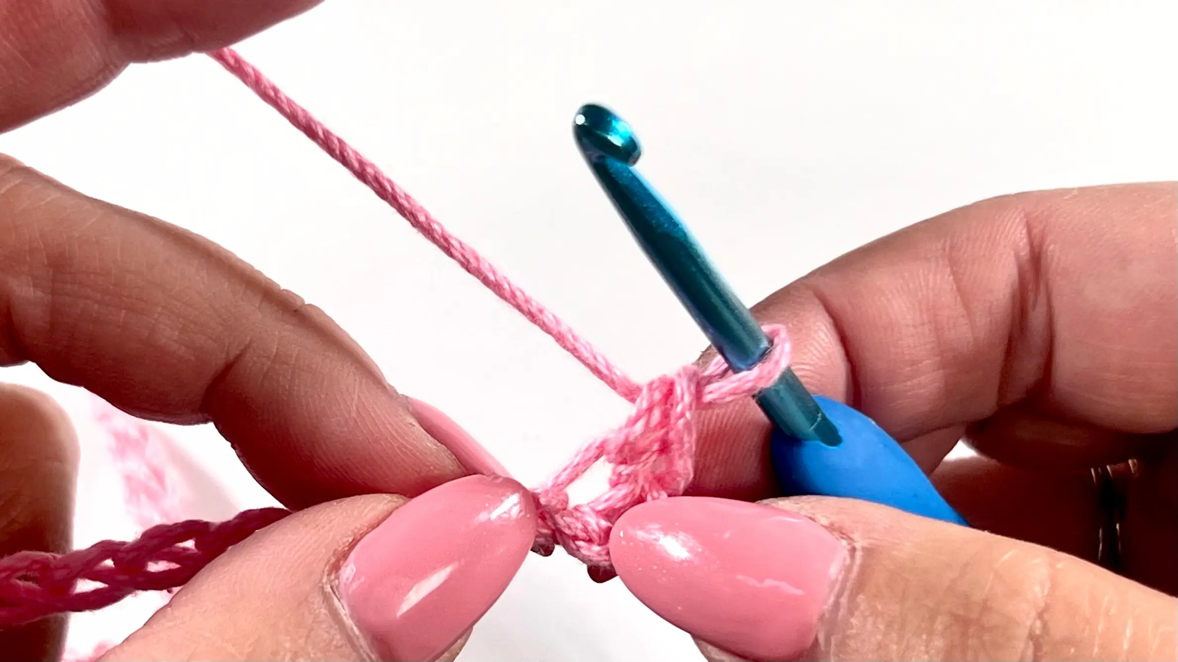 Yarn over and pulling up a loop with blue hook through the pink foundation chain while crocheting the Primrose Stitch.
