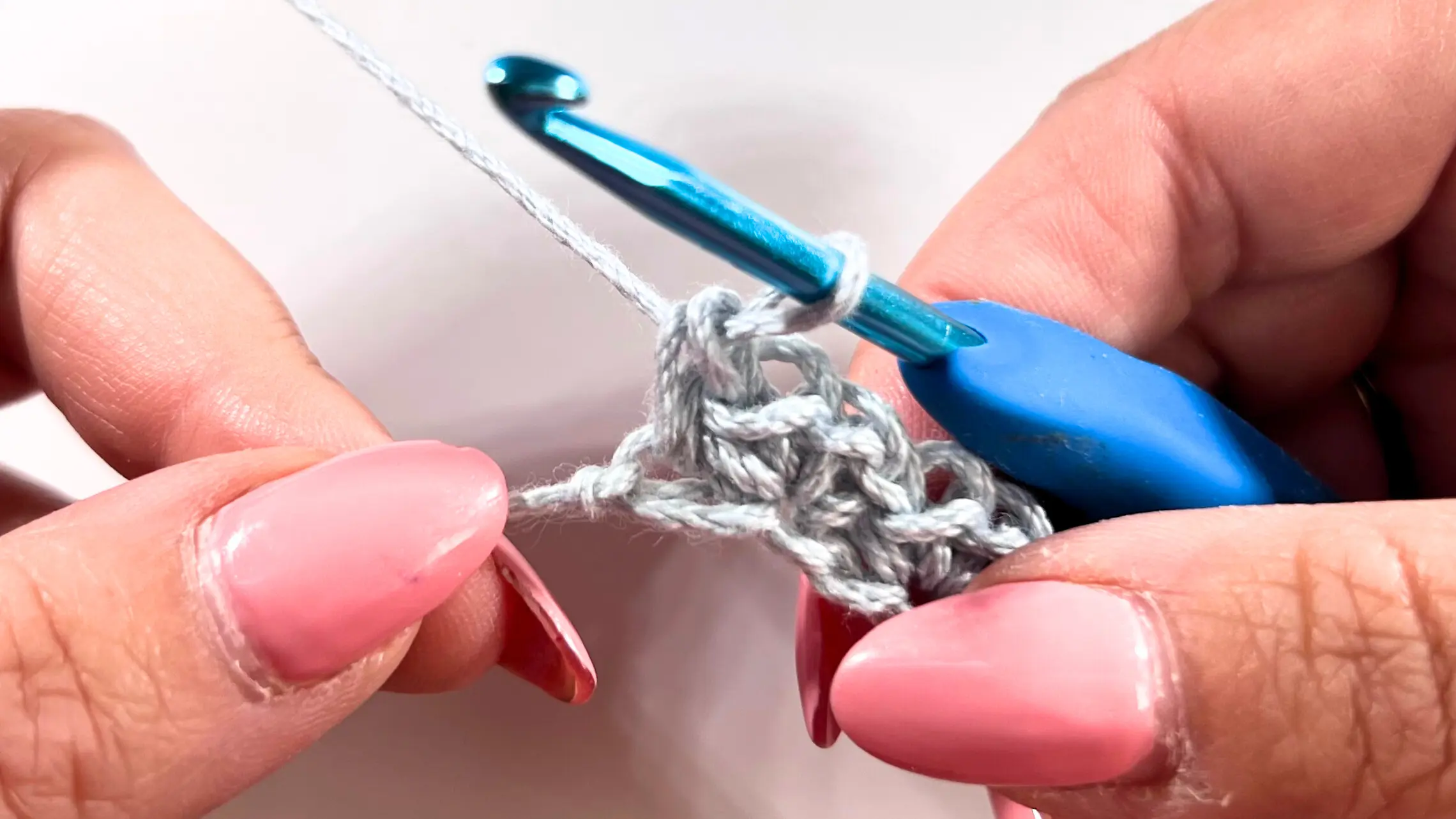 Close-up of hands crocheting into the last stitch of the foundation row, securing the final Spider Stitch with a single crochet. The completed first row is visible below the hook.