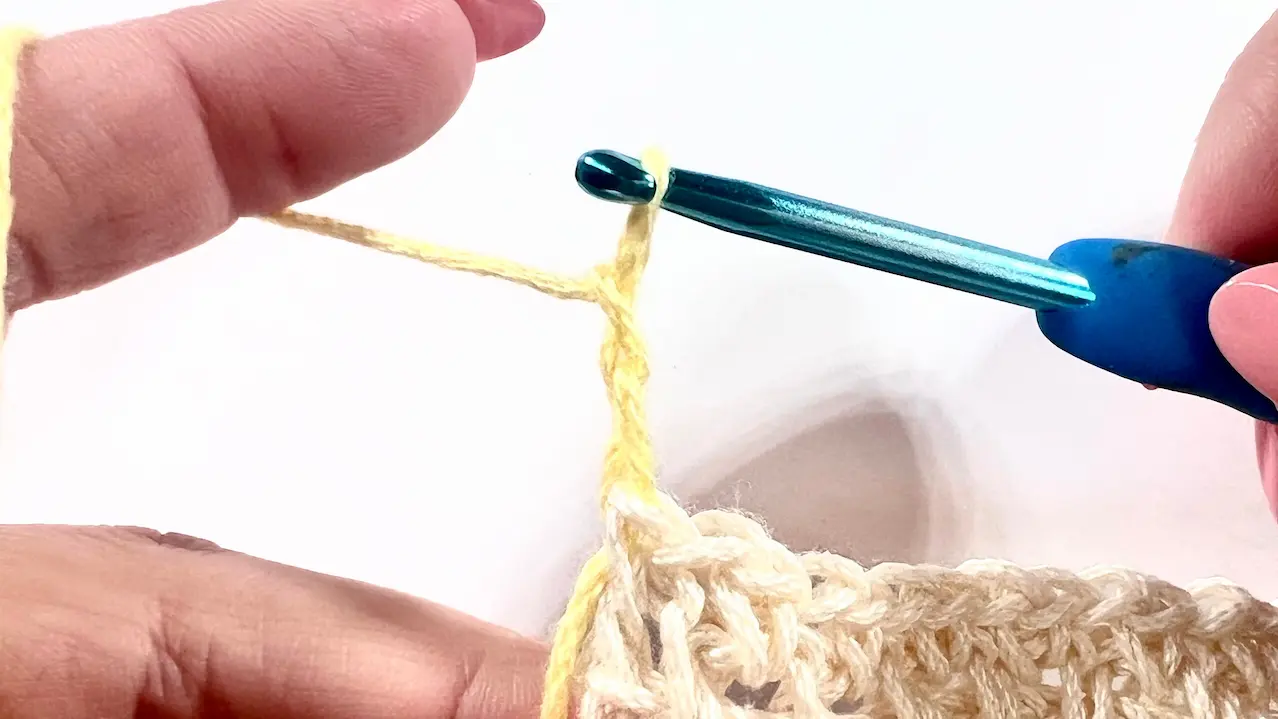Close-up showing a new chain made with yellow yarn after switching colours, ready to continue the next row in single crochet.