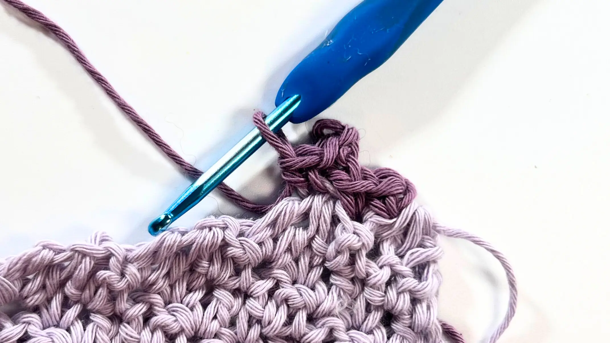 Close-up of a lavender crochet washcloth with a darker purple yarn worked into the edge, beginning the Picot Border scallops.