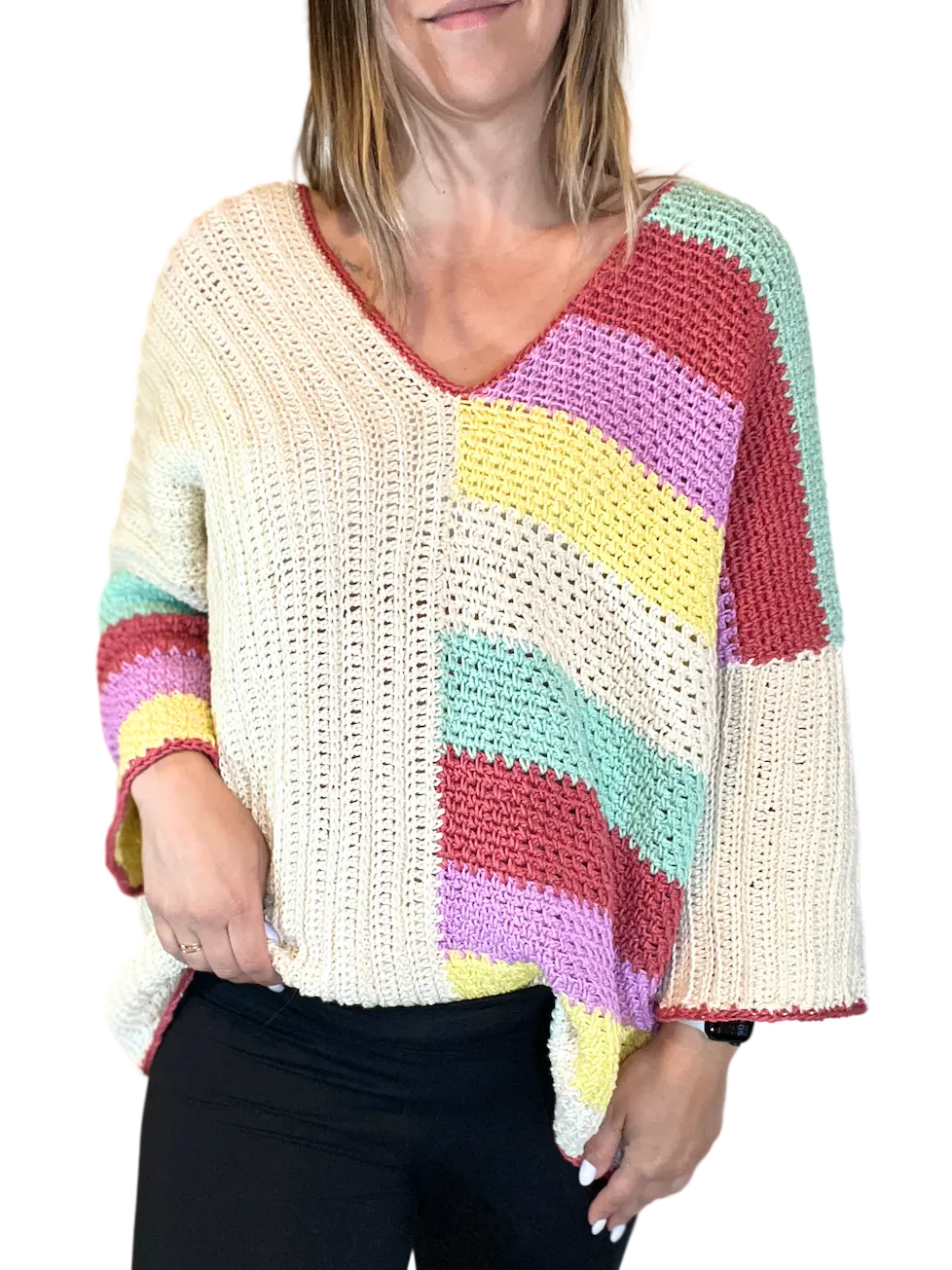 A woman wearing the Happy Stripes Sweater crochet pattern, showing the cozy oversized front panel with a diagonal mix of cream and colourful textured stripes and a V-neck.