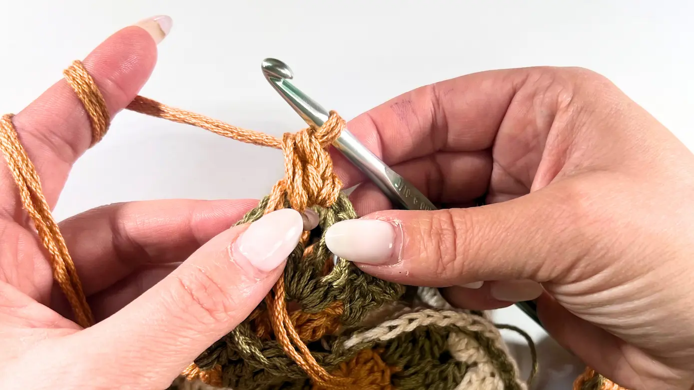 The first single  crochet stitch worked in orange yarn are beginning to form the crochet strap.