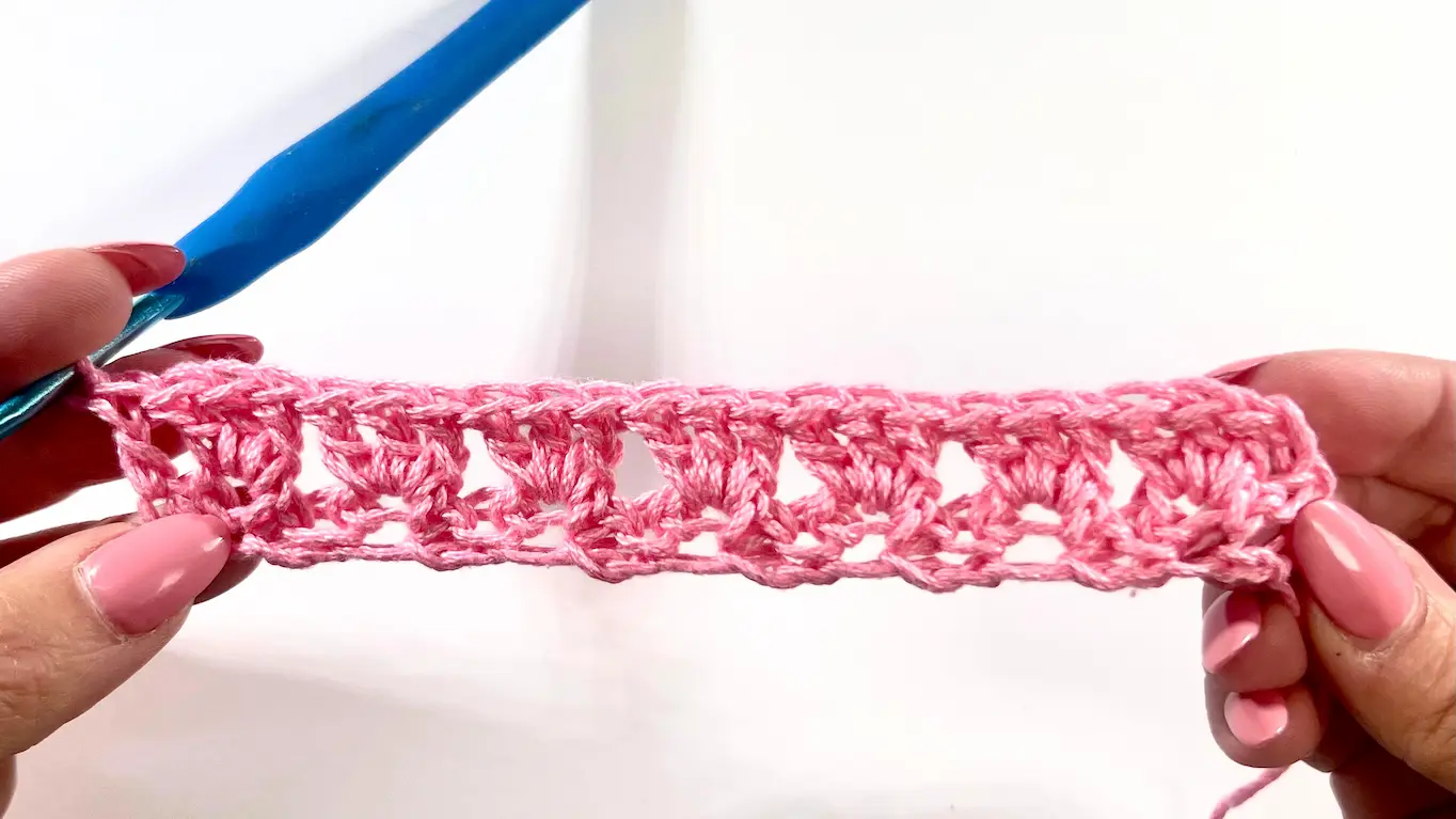 Two completed rows of the Primrose Stitch in pink yarn, displaying the textured clusters formed by the 2-row repeat.