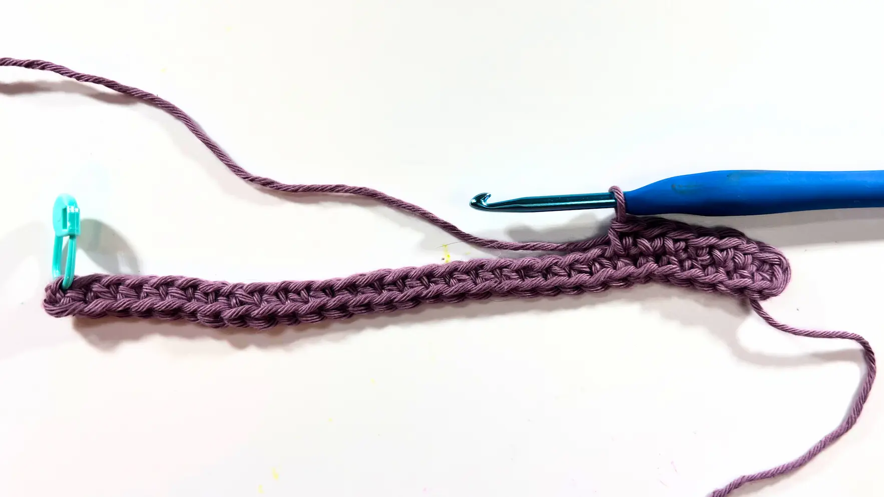 Beginning rows of crochet wall organizer with stitch marker and blue hook.