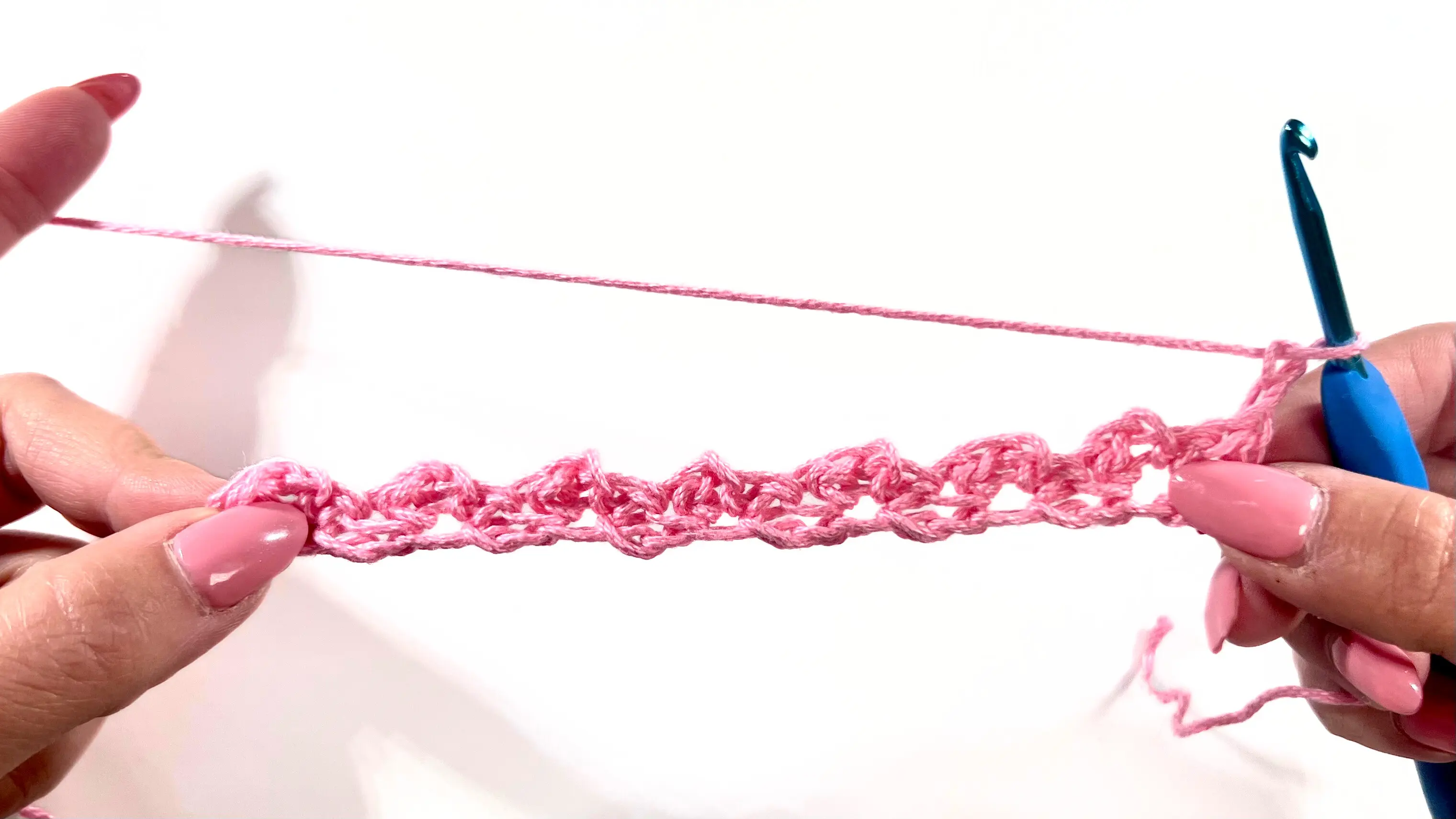 First completed row of the Primrose Stitch pattern shown in pink yarn, highlighting the repeating textured clusters.