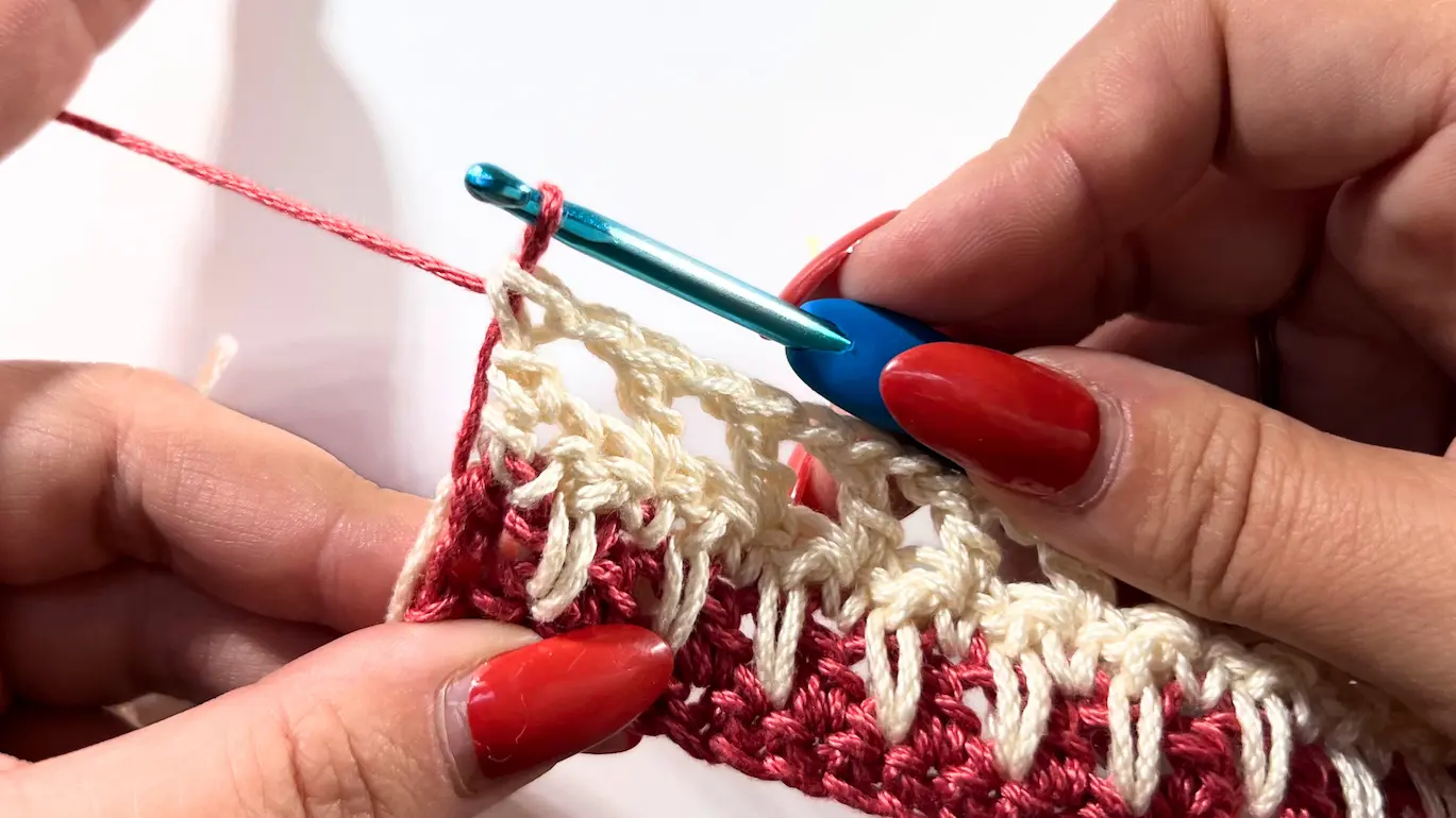 Close-up of crochet hook pulling red yarn through the last two loops of the final double crochet to complete the colour change.