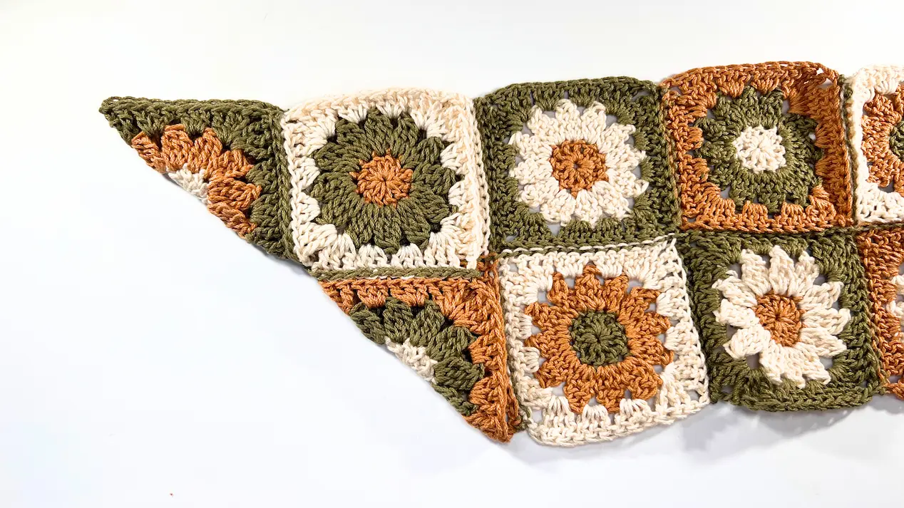 One corner of the crochet daisy square section is folded inward, forming a triangle shape on the left side.