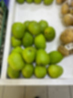 Green mangoes on a white display next to brown potatoes in bags. Neutral, neat arrangement in a supermarket setting. Popular Market stalls in Victoria, Mahe, Seychelles.