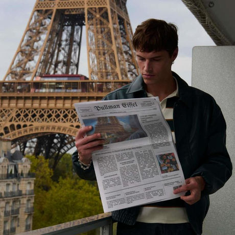 a man holding a newspaper on aterrcae of Pullman our eiffel Paris . The Eiffel tower appears behind him in the background